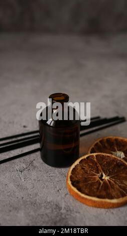 Citrus reed diffuser on dark background. Creating cozy atmosphere at home. Bottle, sticks and dry oranges. Vertical photo Stock Photo