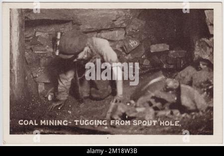 Coal mining - tugging from spout hole: early 20th century photograph of a boy down a pit shaft, dragging a sled behind him whilst crawling on his hands and knees. He is wearing a flat cap and a miners' lamp is hanging from the wall of the seam behind him. The image was one of a set of photos published as postcards by M. Brookes of Pontypridd, South Wales Stock Photo