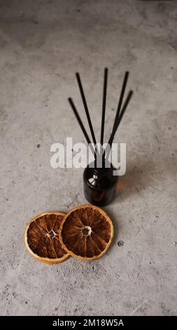 Citrus reed diffuser on dark background. Creating cozy atmosphere at home. Bottle, sticks and dry oranges. Vertical photo Stock Photo