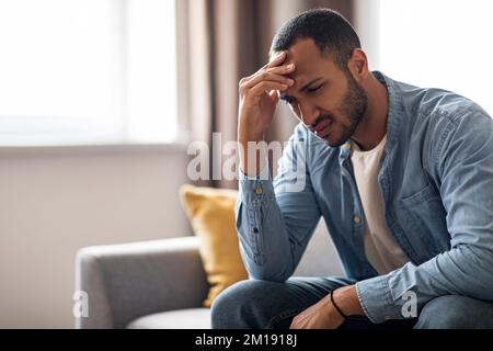 Portrait Of Depressed Young Black Man Sitting On Couch At Home Stock Photo