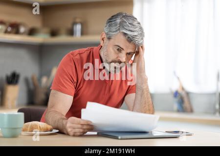 Unhappy middle aged male entrepreneur reading correspondence at home Stock Photo