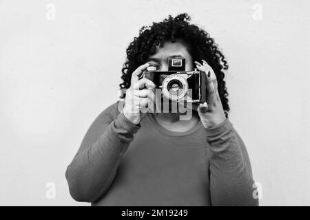 Curvy african woman using vintage camera outdoors in the city - Focus on photocamera lens - Black and white editing Stock Photo