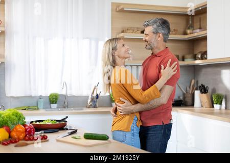 Romantic spouses embracing while preparing meal together at home Stock Photo