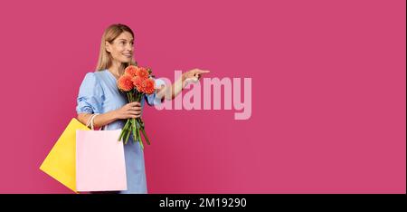 Shocked smiling adult caucasian lady blonde in dress with many packages with purchases and bouquet Stock Photo