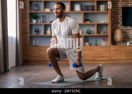 Athletic Black Man Doing Lunges Exercise With Dumbbells While Training At Home Stock Photo