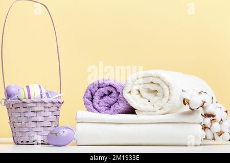 Folded white bed linen, rolls of towels basket with easter eggs on the table Stock Photo