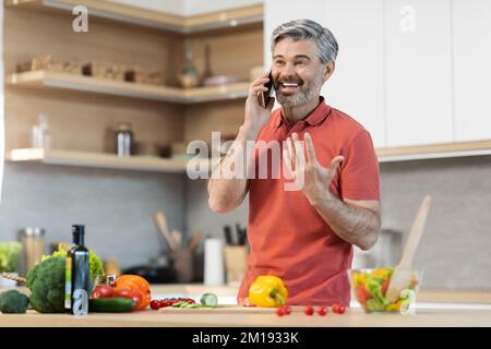 Emotional middle aged man talking on phone while cooking Stock Photo