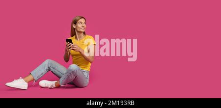 Happy adult caucasian woman blonde in casual typing on smartphone, sits and looks at empty space Stock Photo
