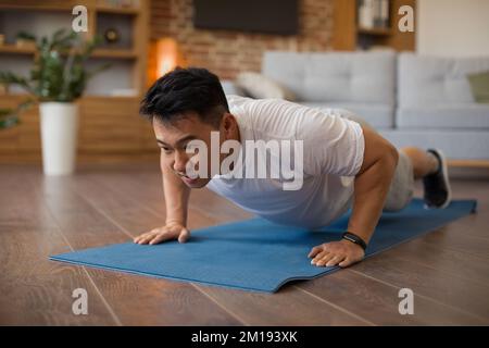 Strong asian mature man making strength workout, doing push ups on sports mat, having domestic workout Stock Photo