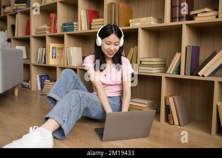 Distance learning. Asian lady in headphones studying with laptop at home, using computer for online education Stock Photo
