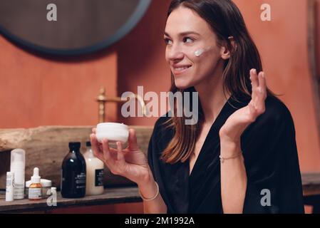 Young woman puts cream on her face. Stock Photo