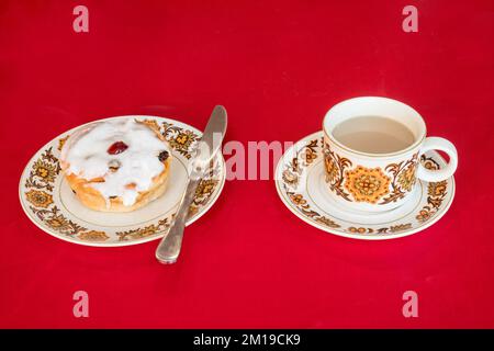 A Belgian bun and a cup of tea against a red background Stock Photo