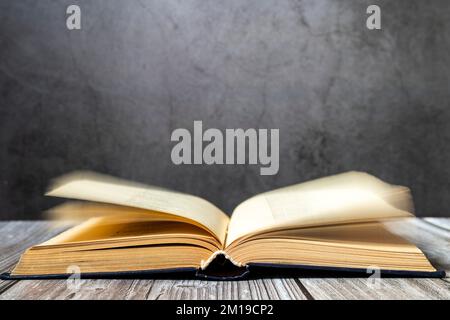 Image of an open antique book on a wooden table with old yellow sheets and dust on a dark background. Side view. Stock Photo
