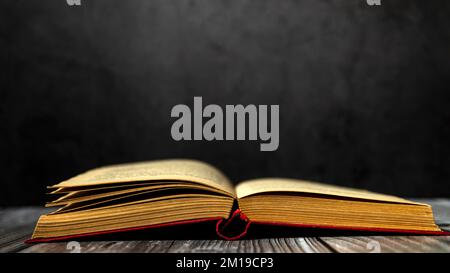 Image of an open antique book on a wooden table with old yellow sheets and dust on a dark background. Side view. Stock Photo