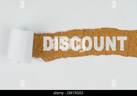 Business and finance. Behind torn white paper on a wooden background the text - DISCOUNT Stock Photo