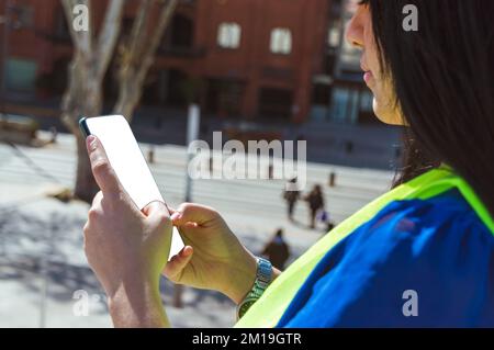 profile view of young caucasian woman in the street watching phone checking notifications, cellphone with blank screen, copy space. Stock Photo