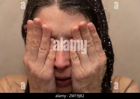 Young woman in shower with her head in her hands. Concept: feeling depressed, bullying victim, bipolar disorder, suicidal, burnout, feeling exhausted Stock Photo