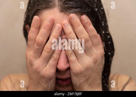 Young woman in shower with her head in her hands. Concept: feeling depressed, bullying victim, bipolar disorder, suicidal, burnout, feeling exhausted Stock Photo