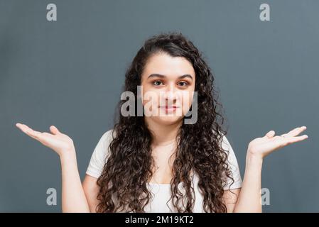 Cheerful young beautiful woman asking, with arms gestures, what happens. Isolated against gray background. Stock Photo