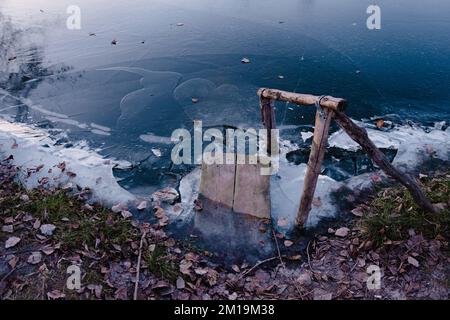 Footbridge in the ice river in early winter. There is some fooliage on a backgroung of the blue ice with air bubbles. Winter landscape scene Stock Photo