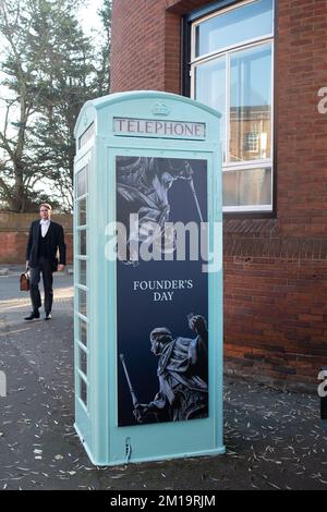 Eton, Windsor, Berkshire, UK. 8th December, 2022. An Eton College Master walks past a former telephone box outside Eton College that has been painted a pale green and had Founder's Day artwork put on it. Each year Eton College celebrate Founder's Day around the Fourth of June. Eton College boys dress in rowing attire and wear boaters with fresh flowers on them and row down the River Thames. Credit: Maureen McLean/Alamy Stock Photo