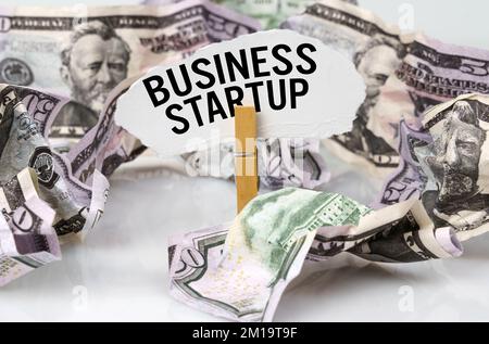 Business and finance concept. There are dollars on the table and there is a clothespin with paper on which it is written - BUSINESS STARTUP Stock Photo