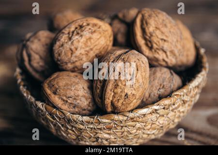 Close-up, whole walnuts in a wicker bowl on a wooden background. Stock Photo