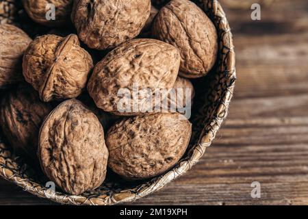 Close-up, whole walnuts in a wicker bowl on a wooden background. Stock Photo