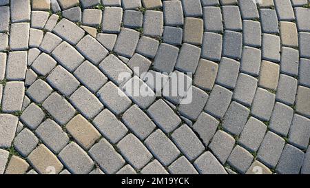 fragment of a paved surface with gray and beige rounded cubic cobblestones overgrown with green grass along the seams as a relief texture Stock Photo