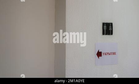 the inscription in Russian "Shelter" on an empty light wall with the emblem of the silhouettes of a man and a woman Stock Photo