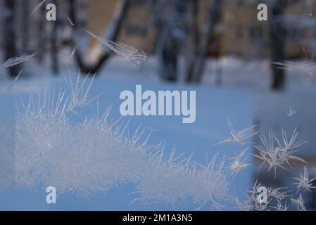 frozen icicle on a window pane on a cold winter day. sunlight shines through the glass in the room, creating the shadows of ice flowers on the wooden Stock Photo