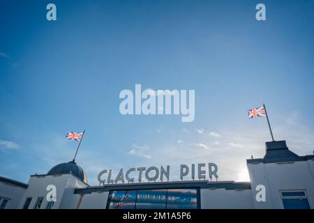 Entrance to Clacton / Clacton-on-Sea pier, with union flags flying over it, against a blue sky with wispy white clouds. Stock Photo