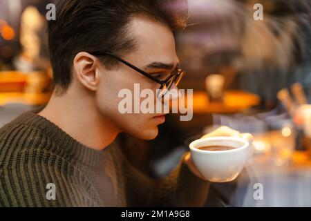 Young white brunette serious man wearing eyeglasses drinking coffee in cafe Stock Photo