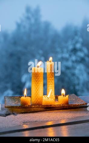 Set of natural rolled beeswax candles from pressed beeswax honeycomb sheet at home balcony outdoors snowy winter forest on background. Hobby concept. Stock Photo