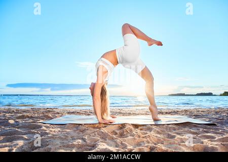 young woman practicing yoga near the river.Wheel pose , Dhanuras Stock Photo