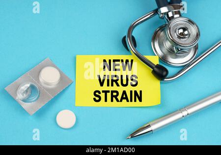 Medical concept. On a blue surface, a stethoscope, pills, a pen and a yellow sticker with the inscription - New virus strain Stock Photo