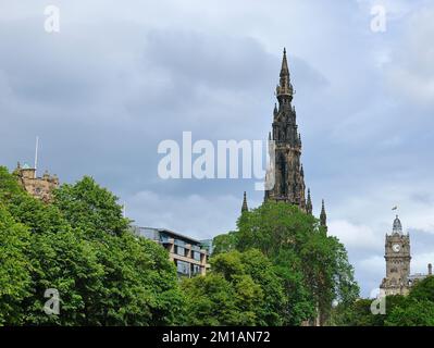 A wide view of the top of the Scott monument, Edinburgh with the Balmoral Hotel clock tower on the background and leafy trees in the foreground Stock Photo