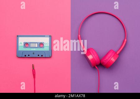 A-side of blue  audio cassette on a pink background and pink headphones on a purple background. Analog audio music concept Stock Photo