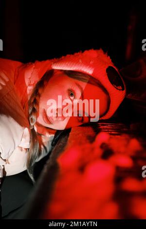 Portrait of young woman pianist in white winter clothes close up in red light with snow on the keys Stock Photo