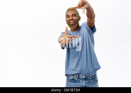 Happy smiling Black man, creative guy looks through hand frames, capture moment, taking photo, stands over white background Stock Photo
