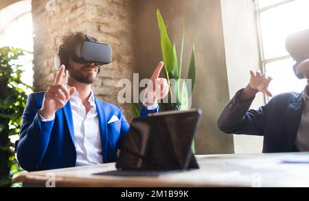 Innovation business team creating a futuristic agency in metaverse. Two persons with virtual reality headsets working in the office. Stock Photo