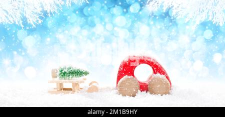 Red Wooden Car Pulling Sled with  Laying Green Christmas Tree in perspective on bright blue bokeh winter background with white snowy branches and fall Stock Photo
