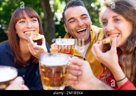Cheerful friends toasting beer glasses outdoors - Group of friends having fun outside in the pub drinking beer Stock Photo