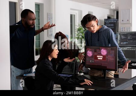 Team of it programmers having web server hacked, looking at critical error on computer monitor in big data office. Diverse software developers trying to solve hacking problem, firewall security. Stock Photo