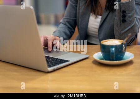 Anonymous female executive using touchpad to scroll data on netbook near cup of latte while sitting at table and working on business project Stock Photo