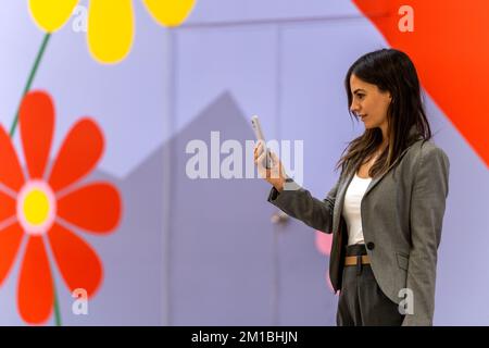 Side view of positive young female manager with long dark hair in formal clothes smiling while having video conversation on mobile phone  Stock Photo
