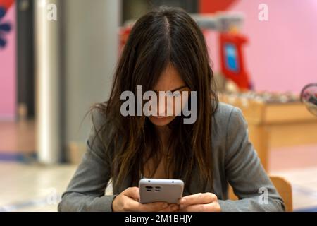 Concentrated young female entrepreneur with long dark hair in formal clothes messaging on mobile phone while sitting in modern cafe Stock Photo