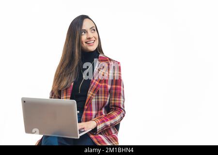 Young adult latin american womoan dressed formaly sitting with laptop computer on her lap looking sideways smiling. White background copy space horizontal studio shot. High quality photo Stock Photo