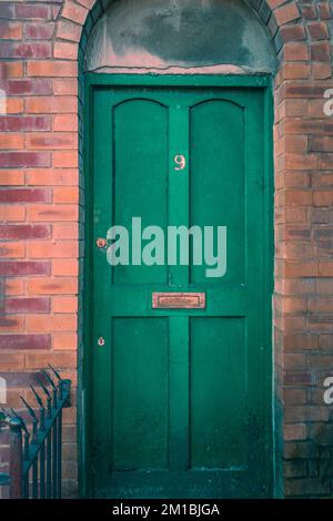 Green entrance door to a house with number nine number sign surrounded by orange and red bricks, England, UK
