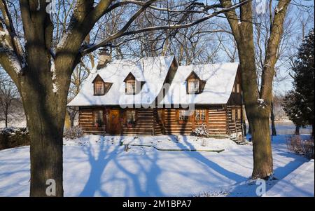 Old 1800s two story Canadiana cottage style log home framed through trees in winter. Stock Photo